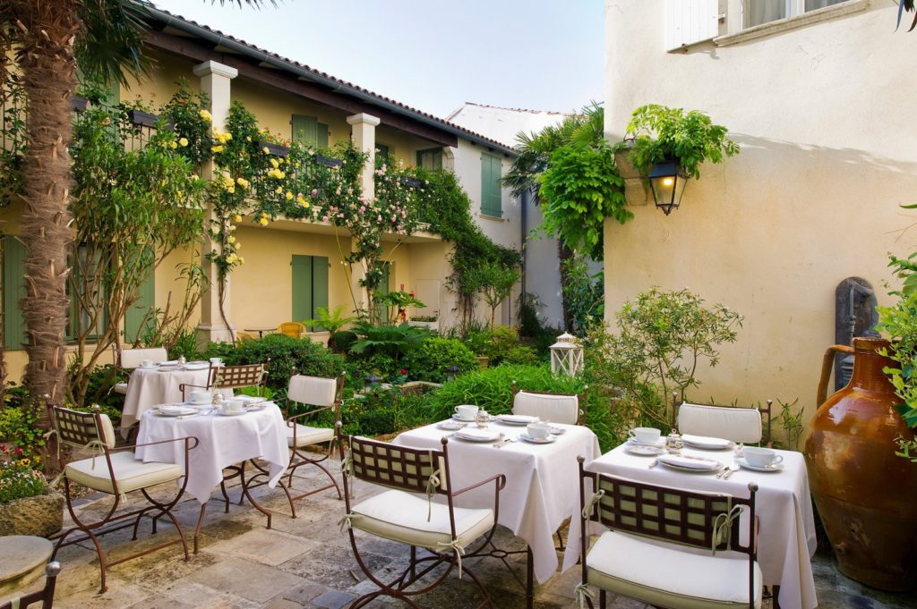 Un patio interior con habitaciones en dos pisos sobre mesas preparadas para una comida.