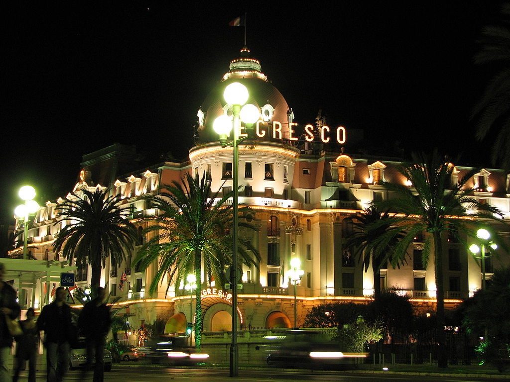 Hotel Negresco en Niza iluminado por la noche con palmeras en primer plano