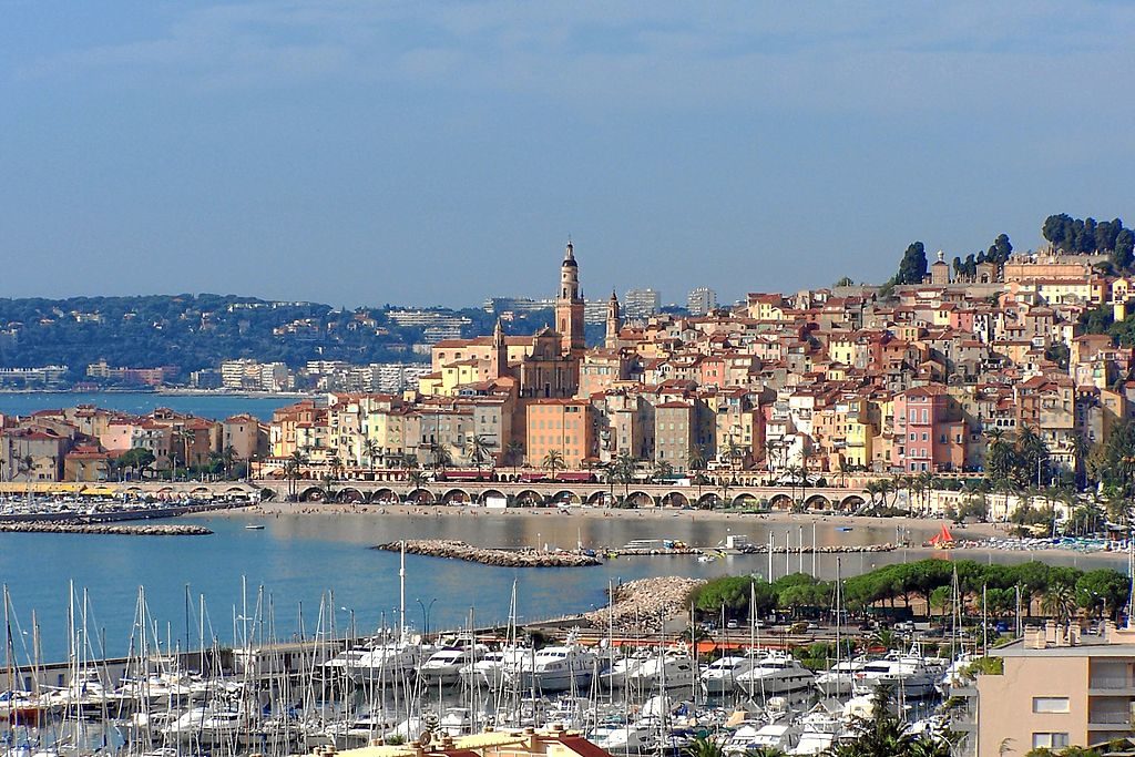 Menton en la colina con casas y torres de colores pastel y yates en el agua