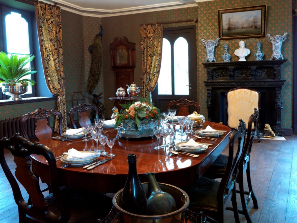 Mesas y sillas victorianas de madera oscura, alfombra azul y cortinas pesadas en el Chateau Hardelot