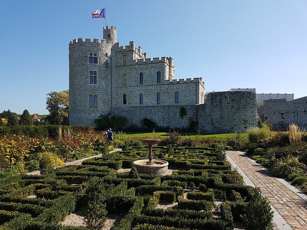 Hardelot Chateau de piedra blanca con una torre alrededor de 3 pisos con bandera ondeando y edificio cuadrado cercano de 1 y 2 pisos. JARDINES DEL PARTERRE DELANTE CASTILLO Y OTRA TORRE Y BANDERA