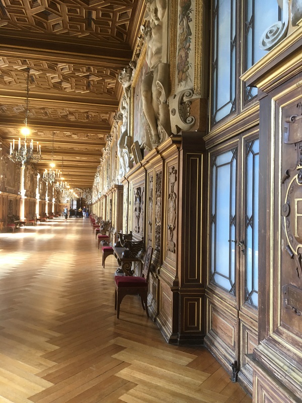 La Gran Galería en Fontainebleau es una galería larga que mira hacia abajo, una pared cubierta con pinturas, repisas y una puerta que se extiende por un piso de madera en la parte trasera.