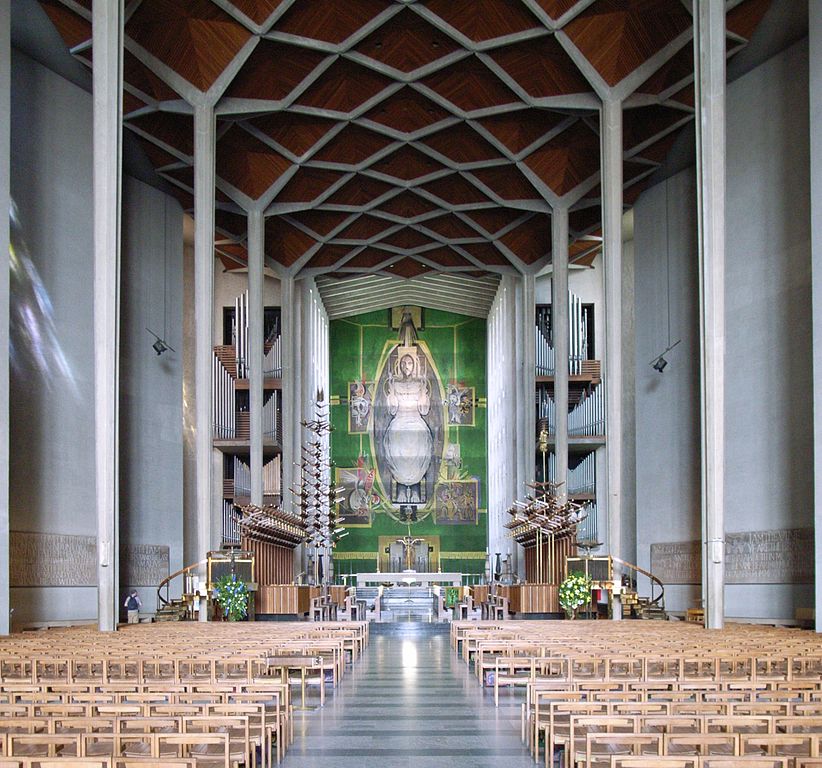 Tapiz de Graham Sutherland en la Catedral de Coventry mirando hacia la nave desde atrás con altos pilares de hormigón en el otro lado y un enorme tapiz de Cristo sobre el altar al final sobre un fondo verde