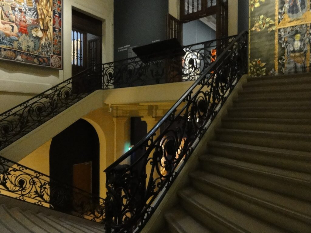 Manufactura des Gobelins que incluye un edificio antiguo y una elegante escalera que conduce a una galería poco