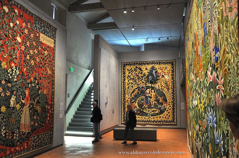 La gran sala principal del Museo Dom Robert muestra a una mujer sentada en un banco mirando enormes tapices colgados en las paredes.