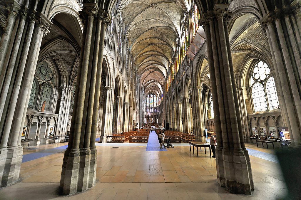 Mirando hacia abajo en la nave de la Basílica de Saint Denis en París mostrando altas columnas que sostienen pasajes abovedados y un techo