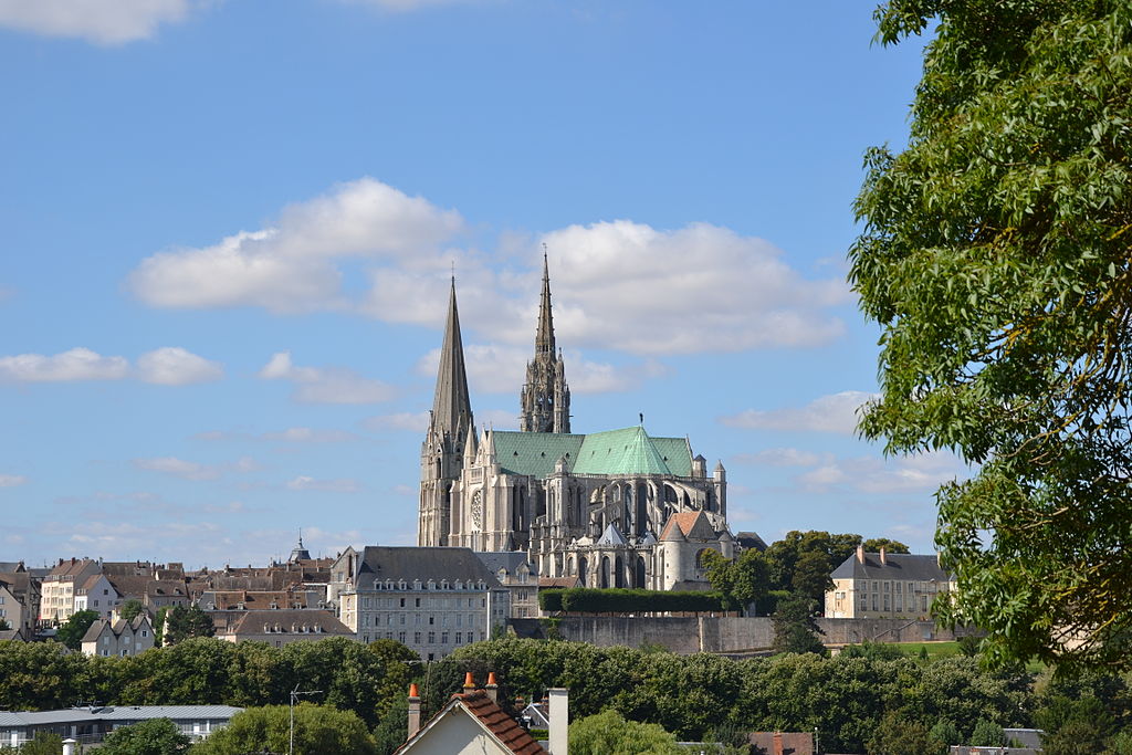 Catedral de Chartres vista desde la distancia en la ciudad de la cima de una colina con árboles a la derecha y nubes detrás de las dos torres