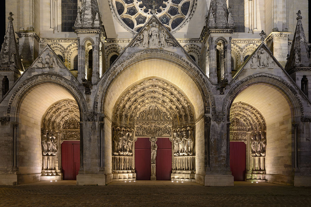 Cerca del frente de la Catedral de Laon con tres puertas principales iluminadas y parte del rosetón arriba desde el exterior