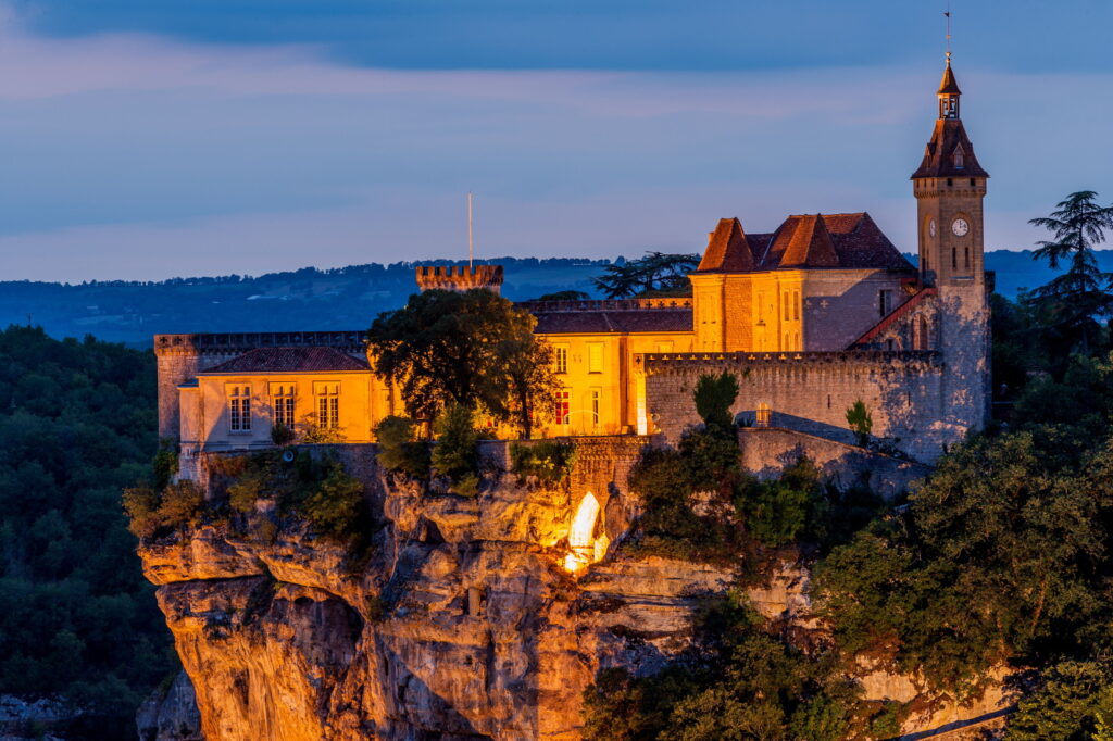 Rocamadour de noche que muestra edificios iluminados en las laderas con un castillo en la parte superior y otros en las laderas