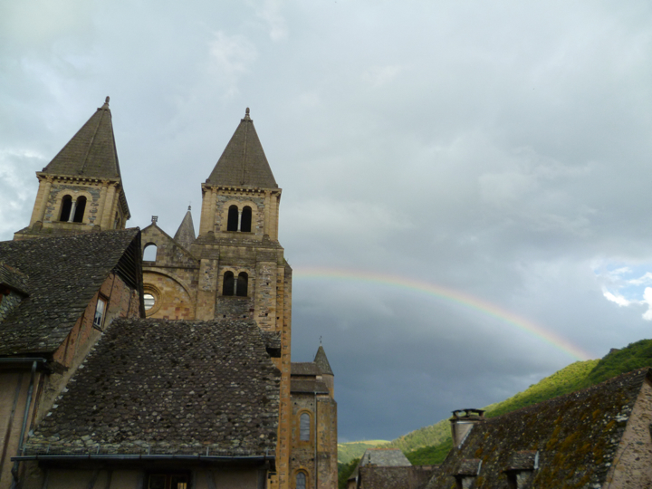 Vista de la Abadía de Sainte Foy al atardecer con un arco iris en el fondo contra dos picos