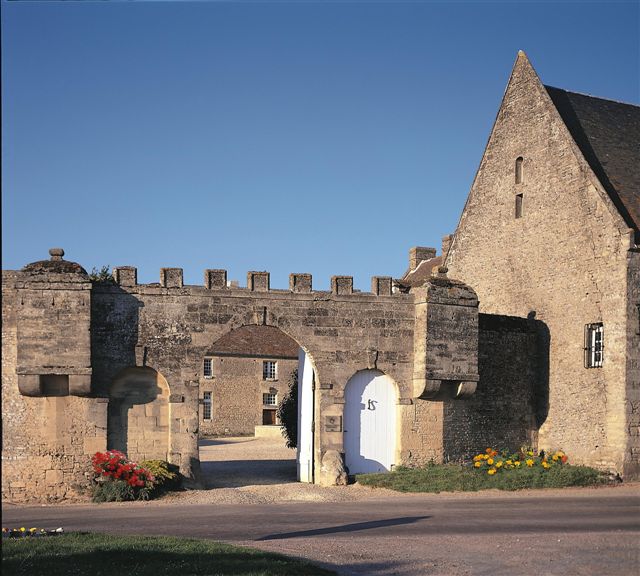 Una puerta en la muralla de un castillo que conduce a La Ferme de la Rançonnière que muestra el edificio a la derecha y en el patio con el edificio en la distancia frente a ti.