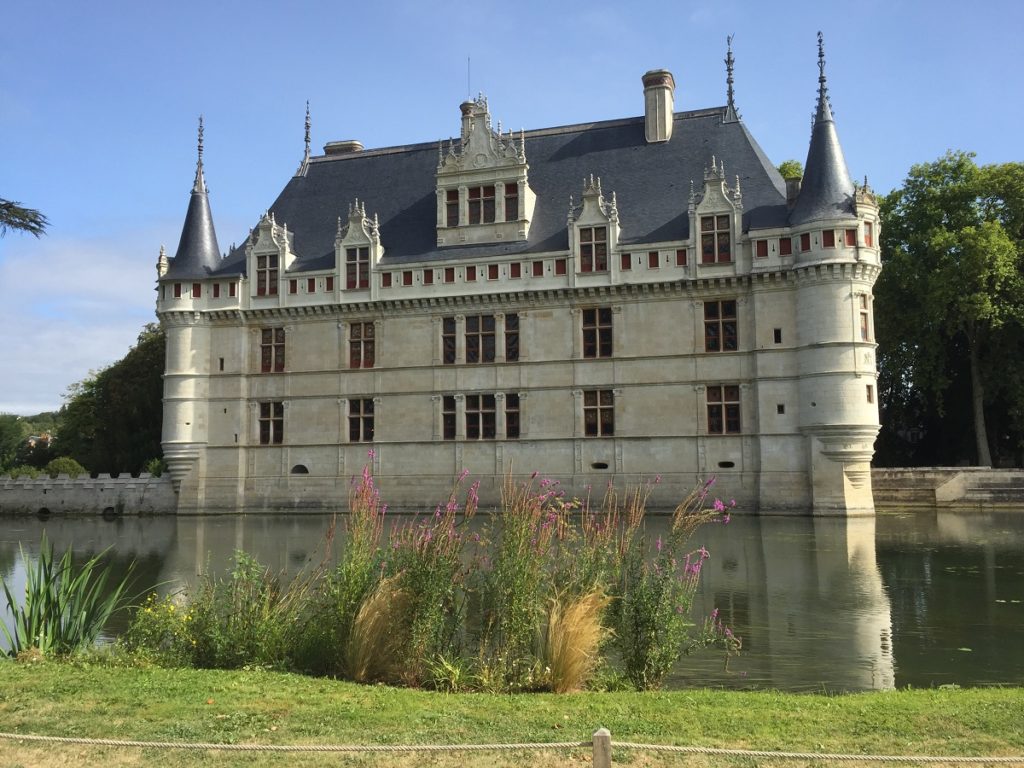 fachada del chateau azay-le-rideau vista desde el otro lado de la motte con torretas, edificio de piedra blanca y vegetación en frente