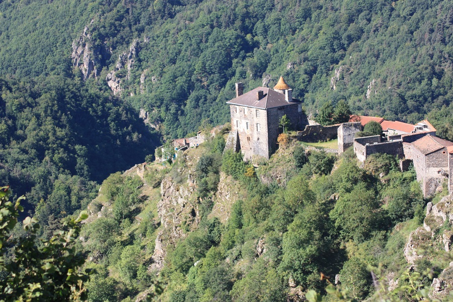 Mirando hacia abajo en un castillo en Auvernia con un castillo de pie en un extremo de un pequeño pueblo y elevándose sobre otro edificio. A lo lejos, las gargantas del río Allier