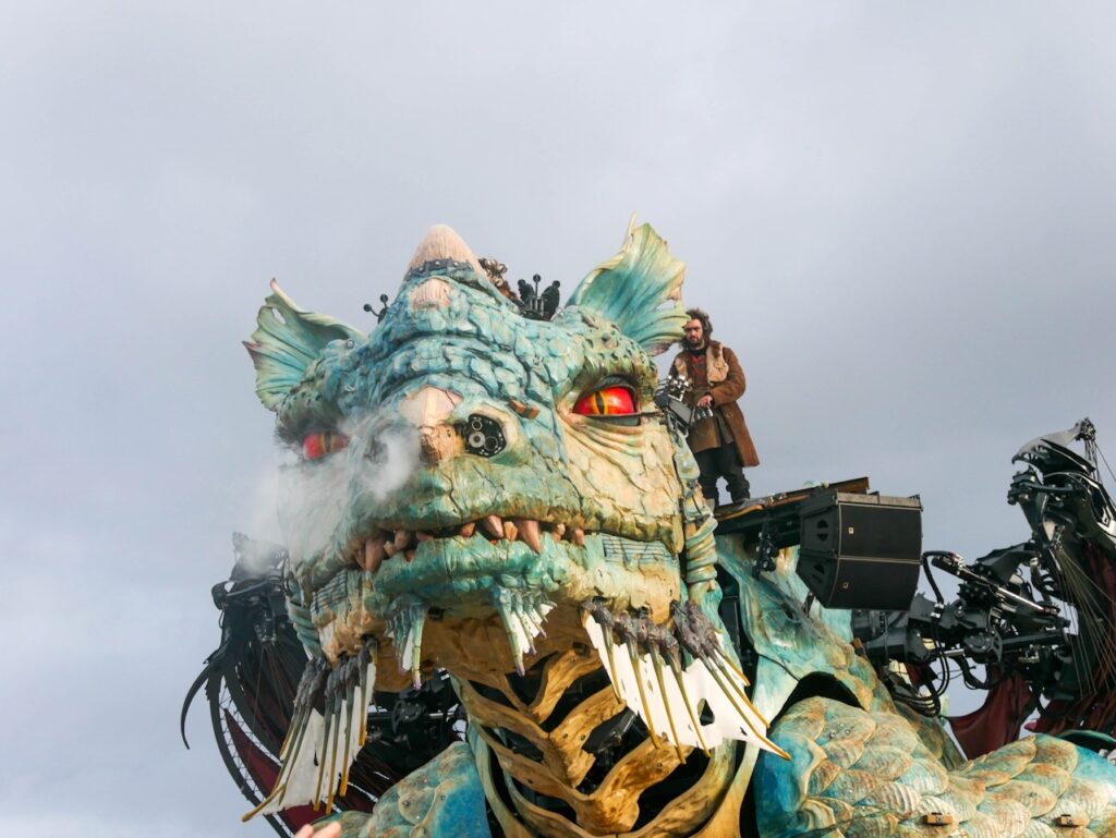 Calais Dragon frente a la cámara con vapor saliendo de las fosas nasales y un hombre encima manipulándolo