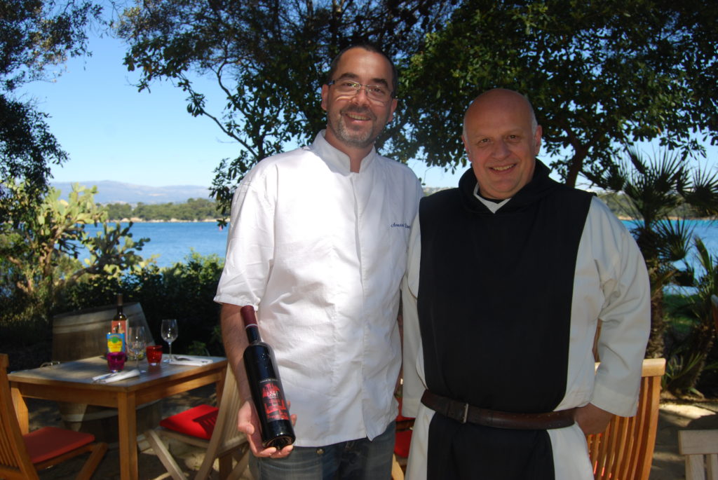 Un monje y un cocinero se paran en St Honorat con el mar y el árbol al fondo.