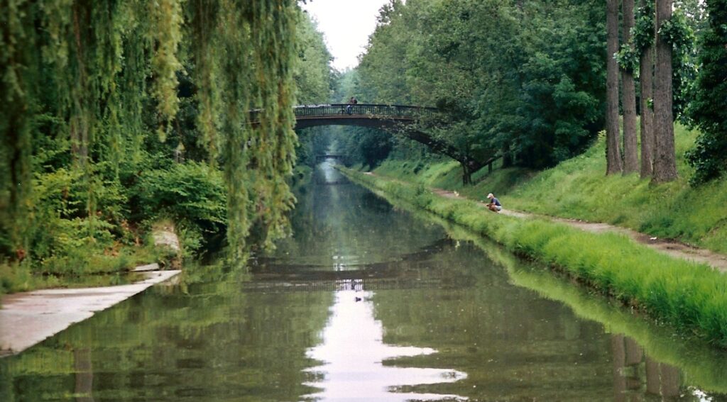 Canal de l'Ourcq mirando hacia abajo a lo largo del tranquilo canal con bancos y árboles a ambos lados y un puente en la distancia