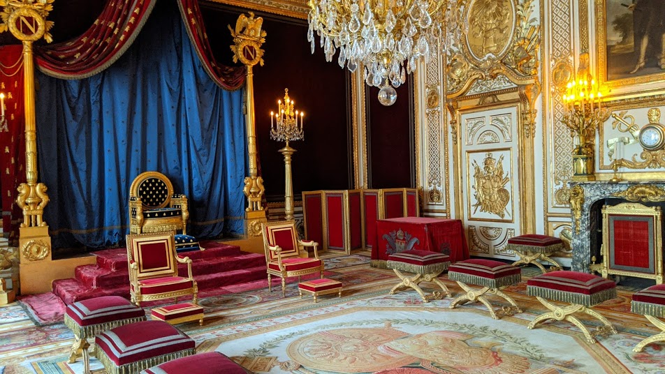 Sala del trono del Imperio francés de Napoleón en Fontainebleau que muestra una decoración elaborada con un enorme candelabro, sillas de terciopelo rojo y un trono modesto