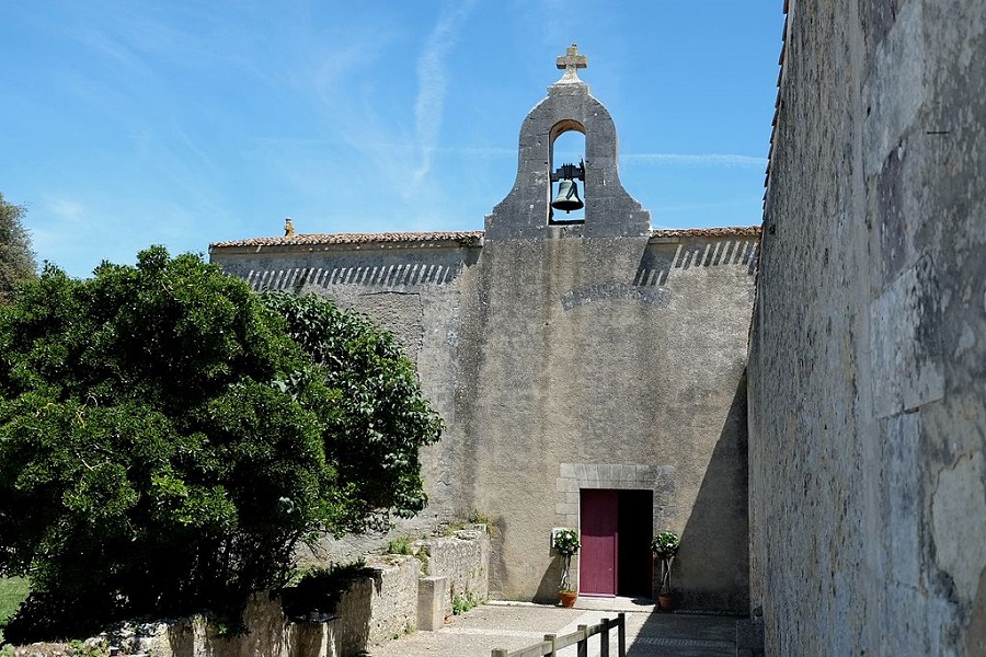 Iglesia de San Martín en Ile d'Aix con altos muros sin ventanas y campanario en el centro y un largo muro de piedra gris a la derecha