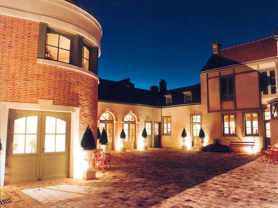 Imagen nocturna de Martel Champagne en Reims con edificios de ladrillo rojo en el patio