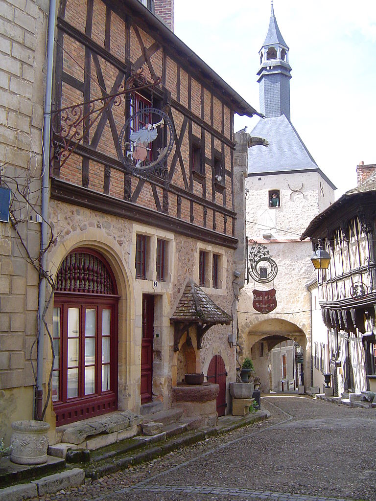 Calle medieval en Bourbon-Lancy con casa de entramado de madera a la izquierda con puerta redonda y ventana de cristal con otra hora de entramado de madera a la derecha que conduce a la torre de la iglesia