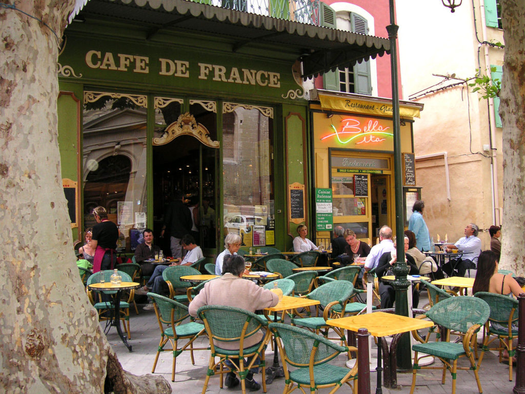 Un restaurante en Isle-sur-la-Sorgue con terraza y mesas, sillas y clientes bajo un dosel en la terraza