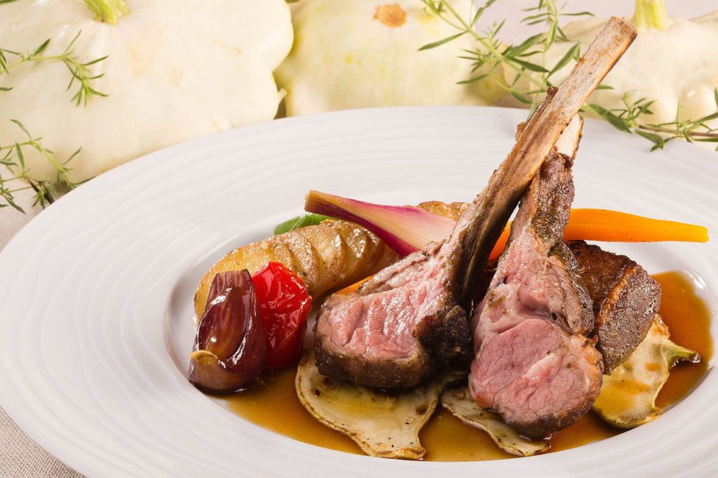 Cortar tiernas chuletas de cordero Sisteron en un plato con verduras de verano