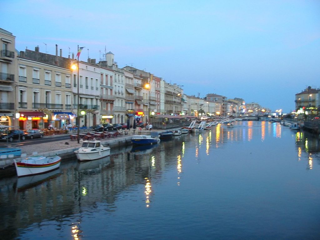 Vista nocturna de Sete con barcos amarrados al mar con lámparas encendidas y restaurantes detrás