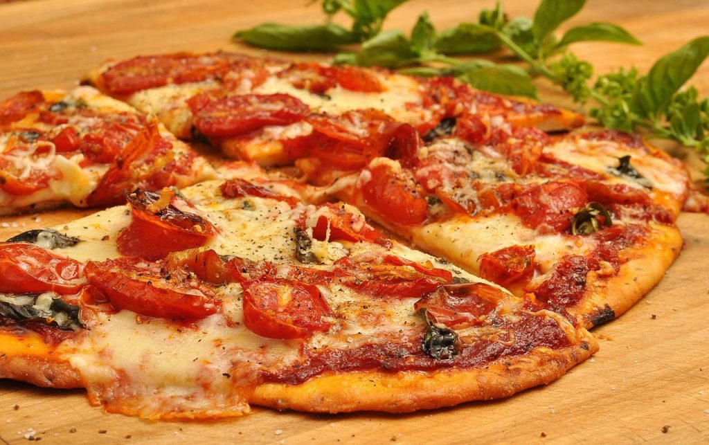 Pizza con tomates y queso en la mesa, cortada con hierba verde en el fondo