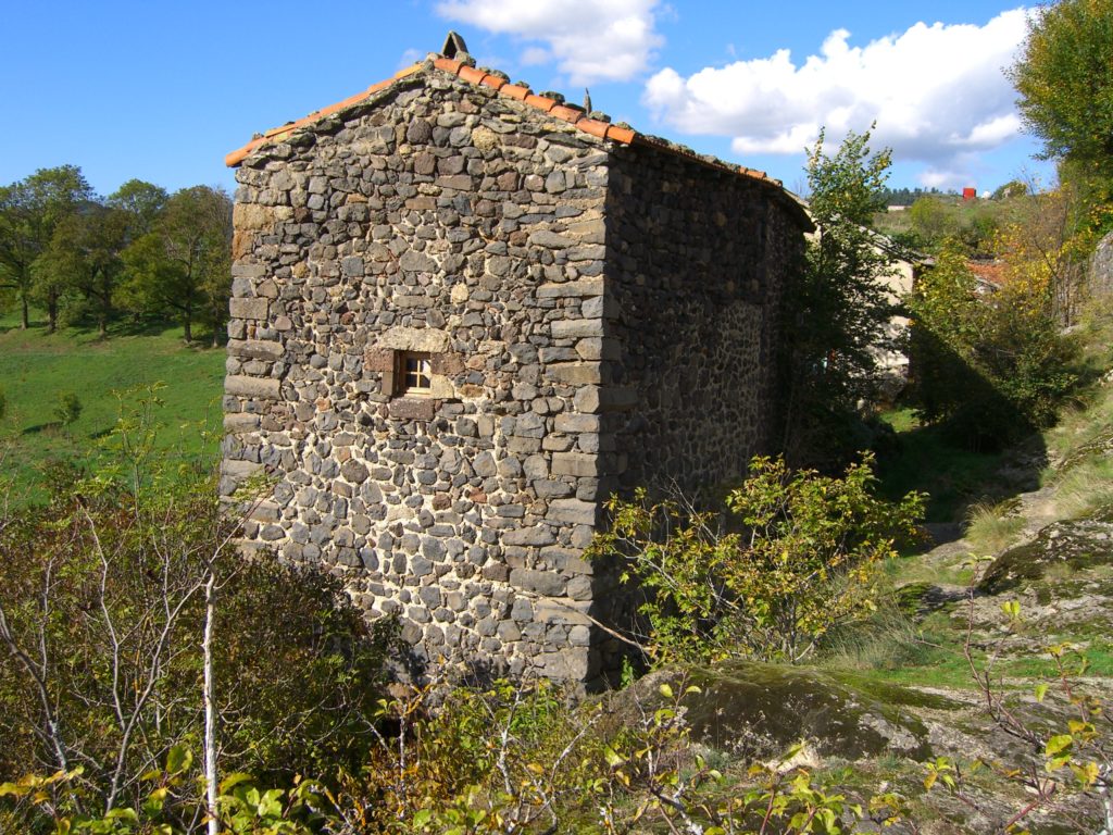 Una antigua casa de piedra con techo de tejas rojas en un pueblo de Auvernia con vistas a las colinas