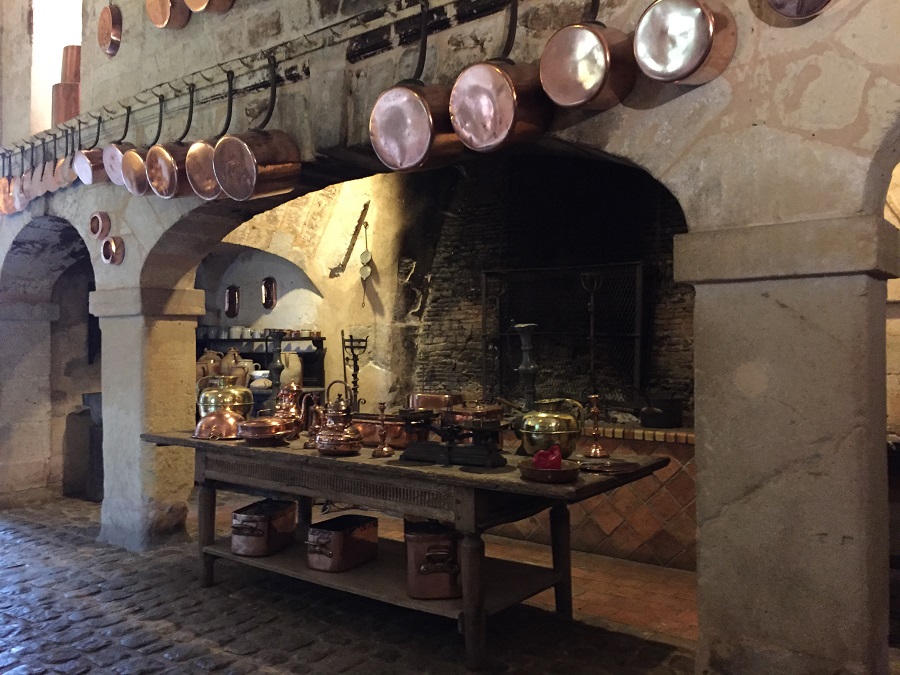 Cocina del Valle del Loira del Château de Brissac. Con ollas de cobre en las paredes, una gran chimenea al fondo y arcos abovedados con una mesa en el centro