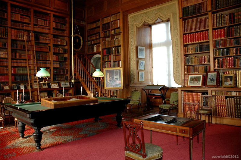 Biblioteca del Valle del Loira Château de Serrant. Una habitación oscura con estanterías que recubren las paredes, una mesa y una silla.