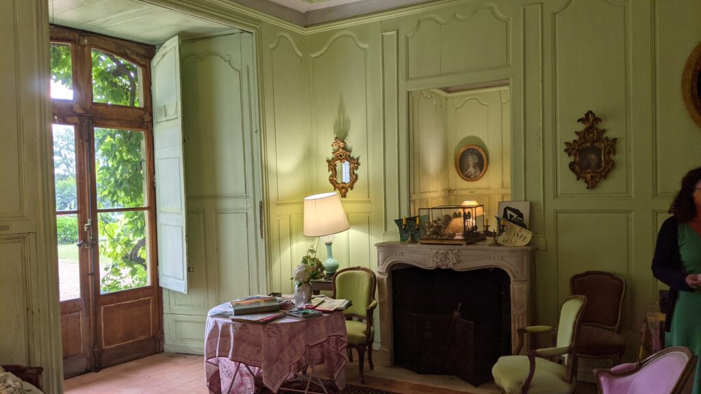 Interior del castillo de Bazouges. Habitación del siglo XVIII decorada con paredes de color verde claro, muebles clásicos y un gran espejo sobre la chimenea con ventanas a la izquierda