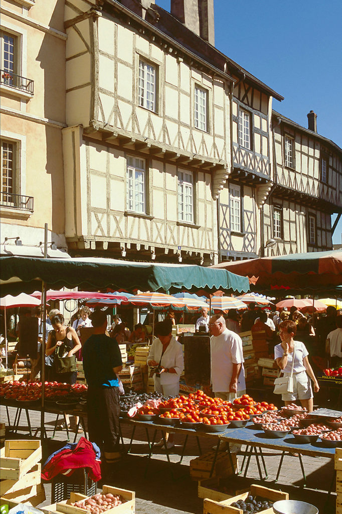 Mercado de Chalon-sur-Saone con antiguas casas de madera al fondo y coloridos puestos de frutas y verduras y gente en primer plano