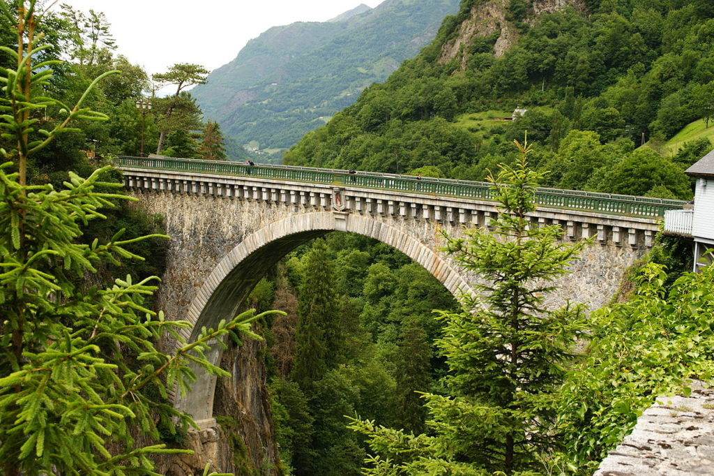 Alto puente de piedra sobre el río en Luz Saint-Sauveur con montañas al fondo