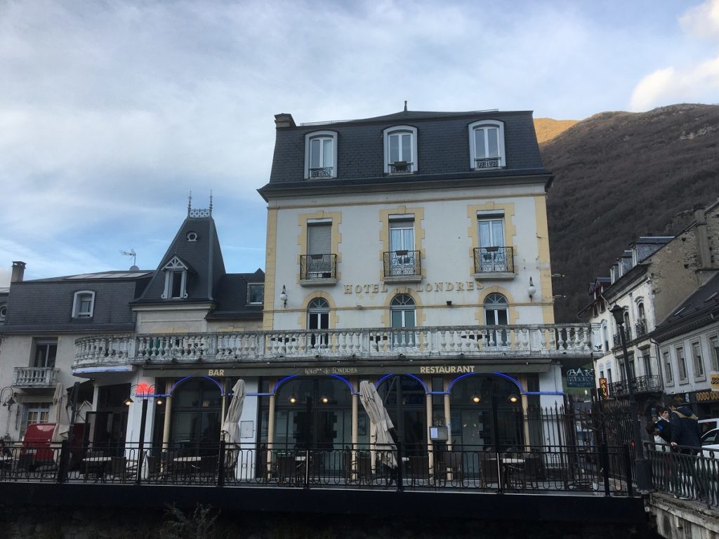 Hotel de Londres en Luz Saint-Sauveur mirándolo con un edificio blanco y una terraza desde la carretera y montañas al fondo