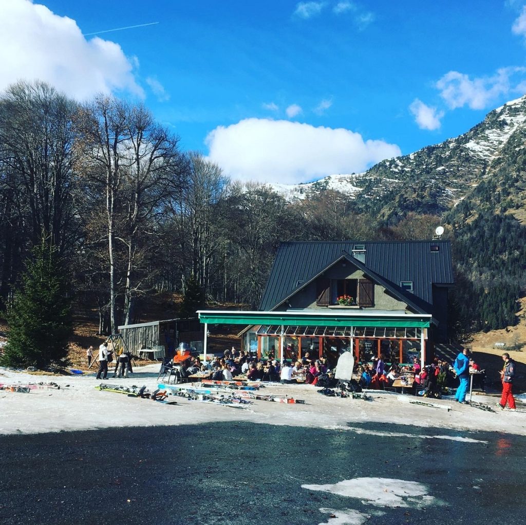 Chez Louisette durante el día al pie de la pista con un restaurante y gente en las mesas de la terraza al aire libre