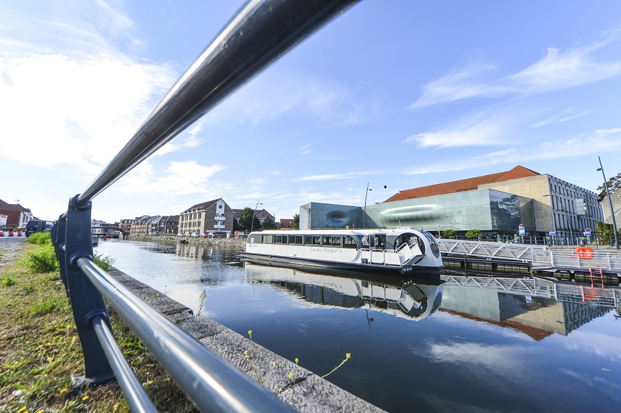 Transporte fluvial gratuito en Calais visto desde la orilla opuesta con un barco en el agua frente al Museo de encaje y moda de Calais