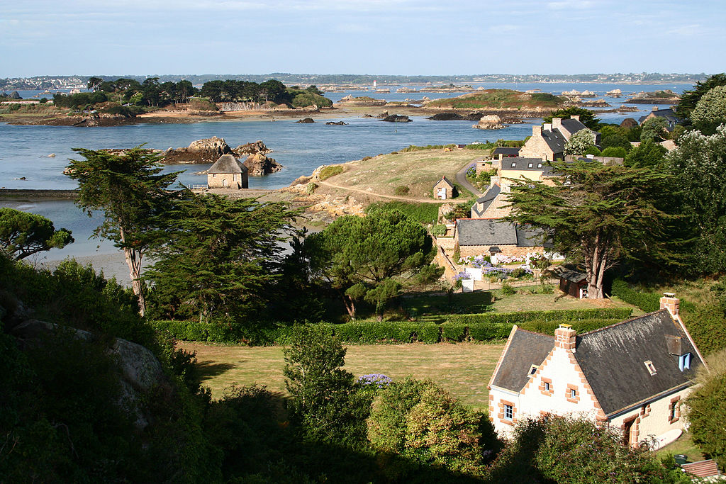 Vista desde lo alto de pequeñas casas de piedra, campos y árboles y el mar al fondo de la bahía