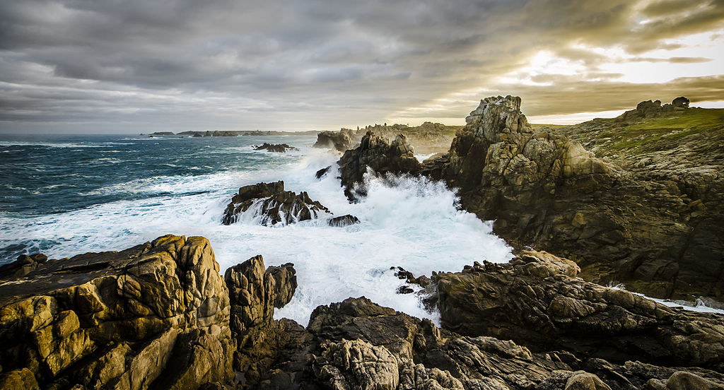 L'Ile de Ouessant Isla galesa en el viento en otoño con olas a la izquierda rompiendo contra rocas en un semicírculo y mar y nubes verdes en el fondo