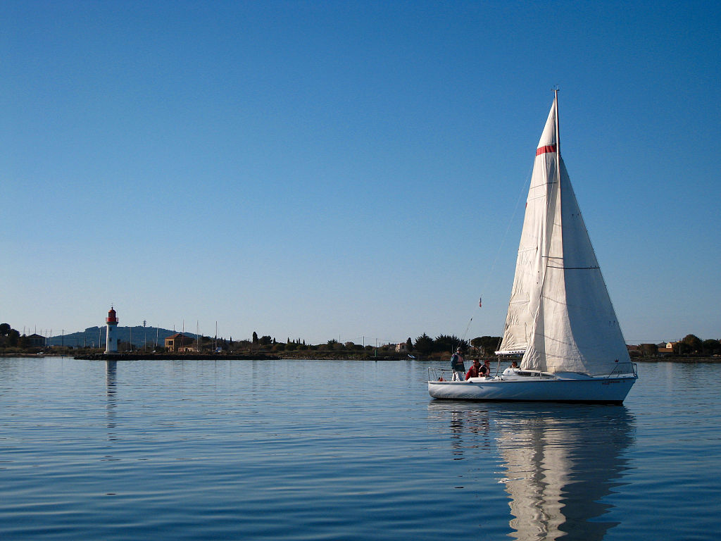 Navegando en las islas Glenan Bretaña con un yate para navegar hacia la derecha en aguas muy tranquilas con una isla baja y edificios al fondo