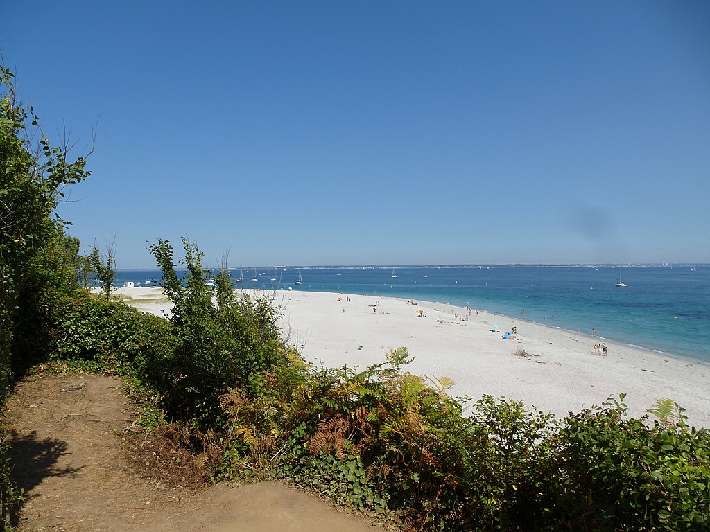 Vista de las islas de la playa Ile de Groix de Bretaña desde las dunas de arena con hierba y aulagas que muestran una larga playa de arena blanca en forma de arco y el mar azul más allá