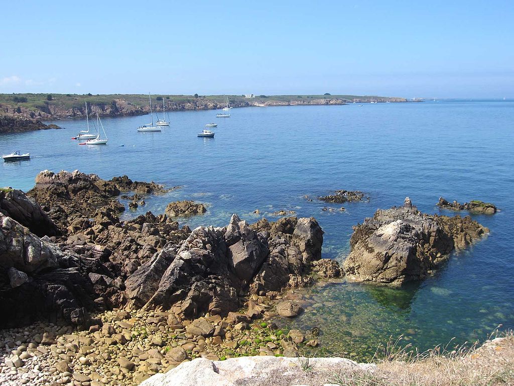 Vista de Ile de Houat desde la orilla con rocas frente a la gran bahía con yates y botes y un promontorio rocoso que se encrespa alrededor