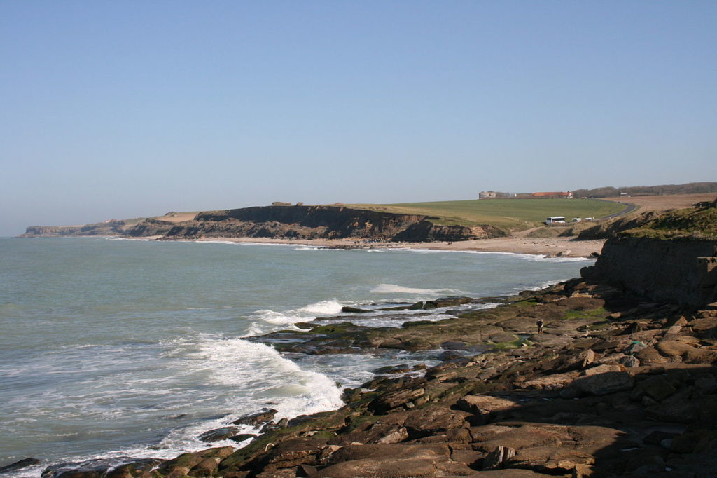 Audresselles en el norte de Francia con una costa rocosa a la derecha que se extiende hasta una bahía de arena con el mar lamiendo las rocas