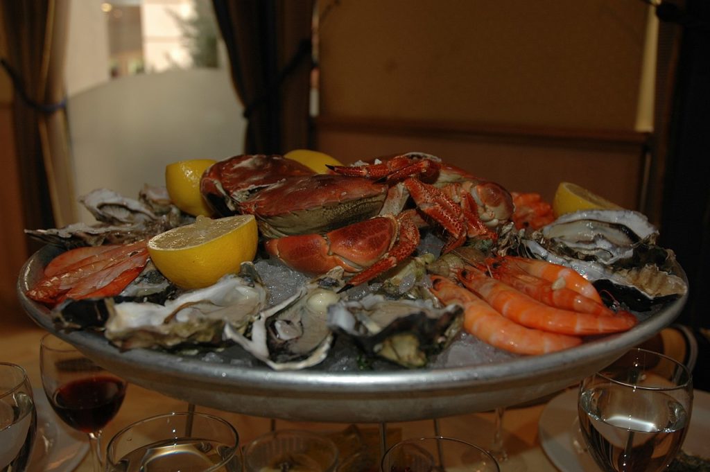 Mariscada con langosta, cangrejos, limón, algas y ostras en una placa de metal sobre una mesa de madera