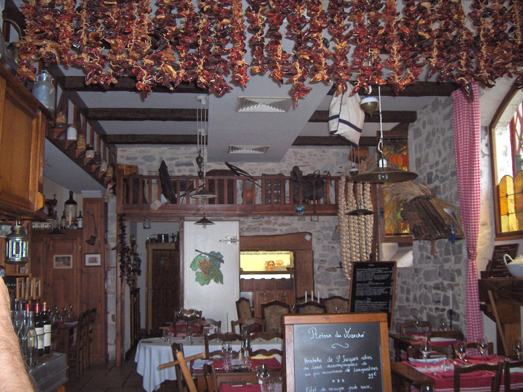 Pimientos secándose en Bayona colgando del techo de un restaurante con un menú de pizarra delante