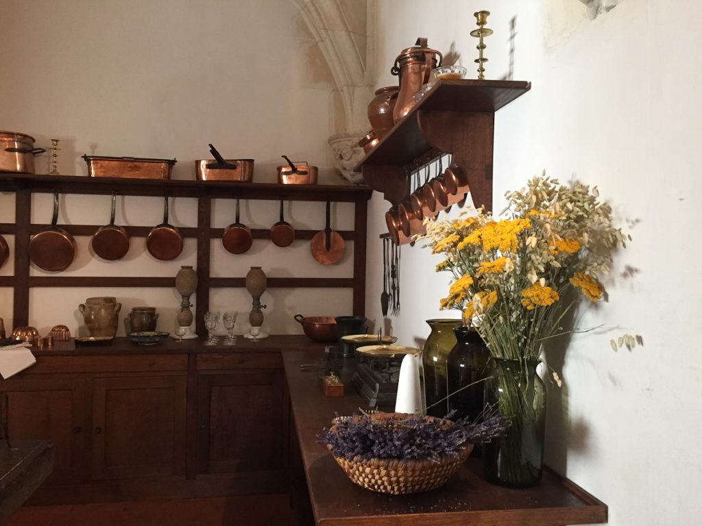 cocinas azay-le-Rideau con ramos de flores en el frente y estantes y clavijas de madera antiguos con ollas y sartenes de cobre brillante