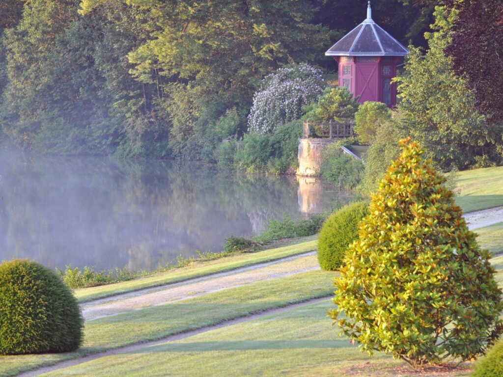 Château du Lude Loir Valley Jardin de la Foinse con agua al fondo, un pequeño y hermoso pabellón junto al agua y los árboles y un césped verde a la derecha