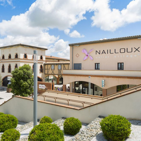 Vista a largo plazo de edificios de 3 plantas en el pueblo outlet de Nailloux. Estilo colonial con vegetación al frente