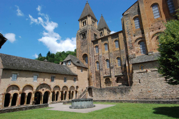 Los campaneros de la Abadía de St Foy en caracolas mirando a través del césped verde en los claustros de arcade izquierdos cerca del lado de la Abadía