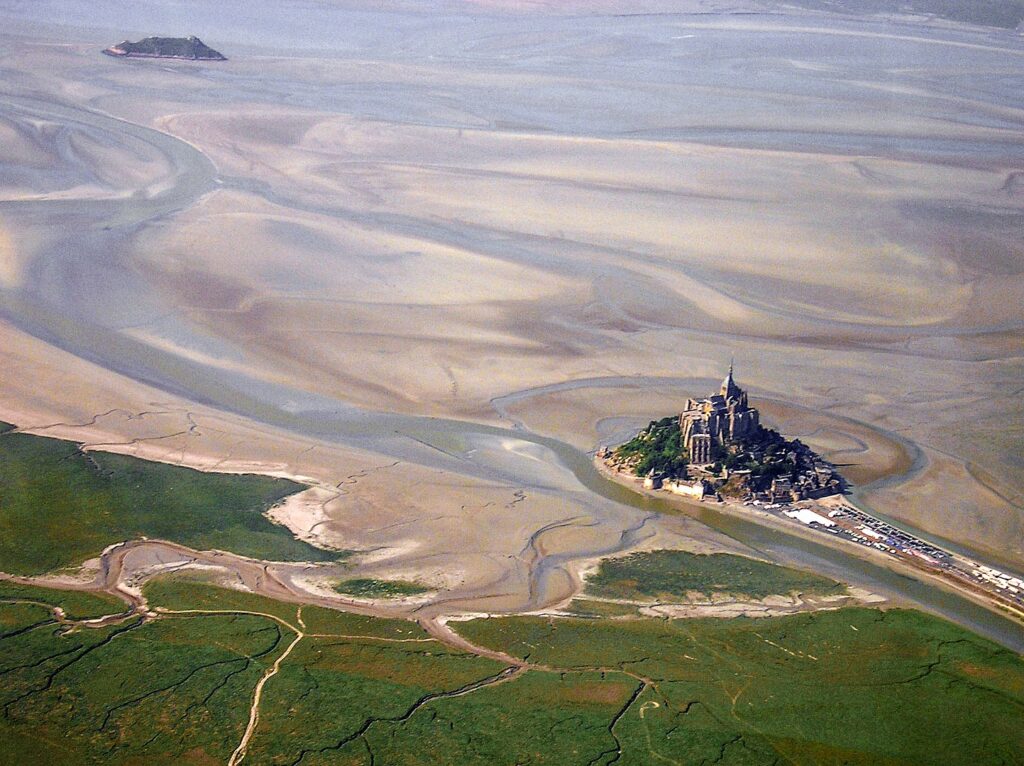 Toma aérea muy larga del Mont St Michel en Normandía que muestra bancos de arena y mar y tierra firme verde y la isla abandonada del Mont St Michel